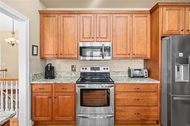 kitchen with stainless steel appliances, tasteful backsplash, light stone countertops, and decorative light fixtures