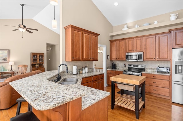 kitchen with sink, stainless steel appliances, light stone countertops, a kitchen bar, and kitchen peninsula