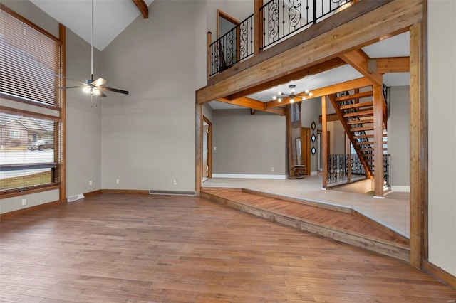 unfurnished living room with beamed ceiling, stairway, wood finished floors, and baseboards