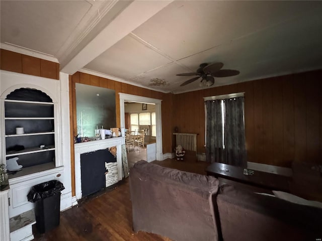 living room with built in shelves, ceiling fan, dark wood-type flooring, wood walls, and crown molding