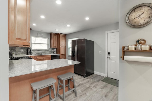 kitchen featuring stainless steel refrigerator with ice dispenser, a breakfast bar, black dishwasher, kitchen peninsula, and backsplash