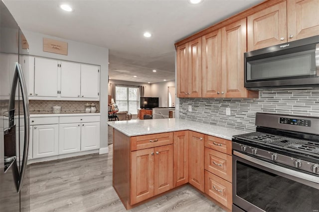 kitchen featuring backsplash, light hardwood / wood-style floors, gas stove, black fridge, and kitchen peninsula