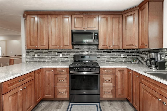 kitchen featuring stainless steel range with gas stovetop, decorative backsplash, light stone counters, and light hardwood / wood-style floors