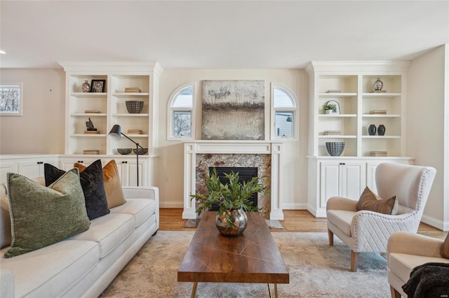 living room featuring a high end fireplace, built in features, light wood-type flooring, and baseboards