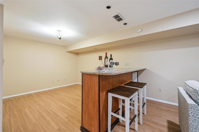 bar featuring a bar, light wood-style floors, visible vents, and baseboards