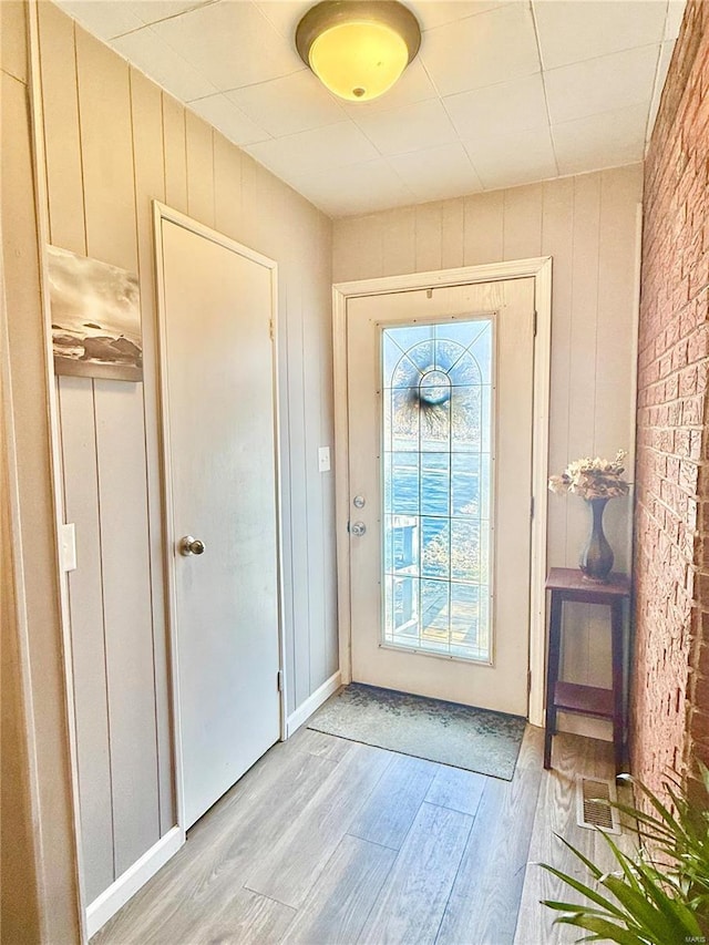 doorway with light wood-style floors, brick wall, and wooden walls