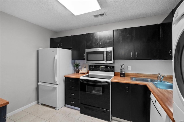 kitchen with sink, light tile patterned floors, a textured ceiling, and white appliances