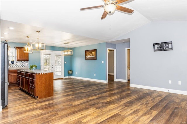 kitchen featuring dark wood-type flooring, light stone counters, hanging light fixtures, stainless steel fridge, and a kitchen island