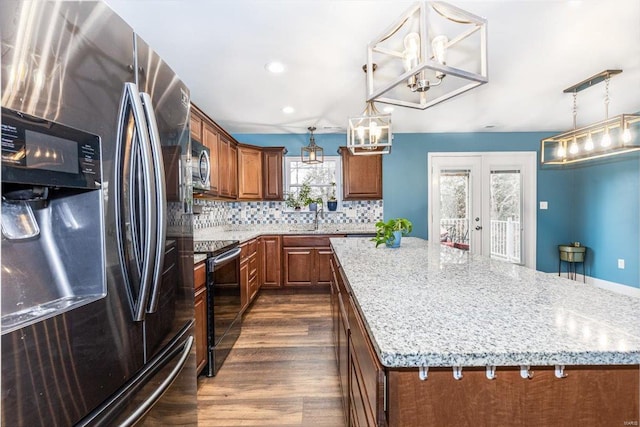 kitchen with light stone counters, appliances with stainless steel finishes, a kitchen island, pendant lighting, and decorative backsplash