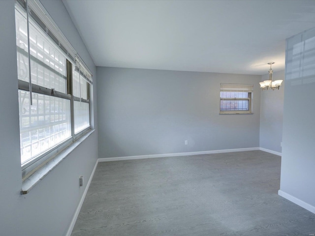 unfurnished room with an inviting chandelier, plenty of natural light, and hardwood / wood-style floors