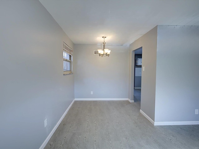 unfurnished room featuring a notable chandelier and light wood-type flooring