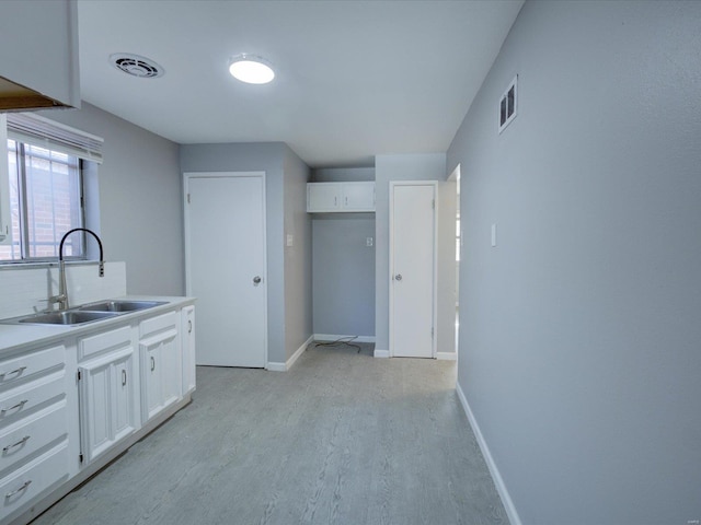 kitchen featuring sink, backsplash, light hardwood / wood-style floors, and white cabinets