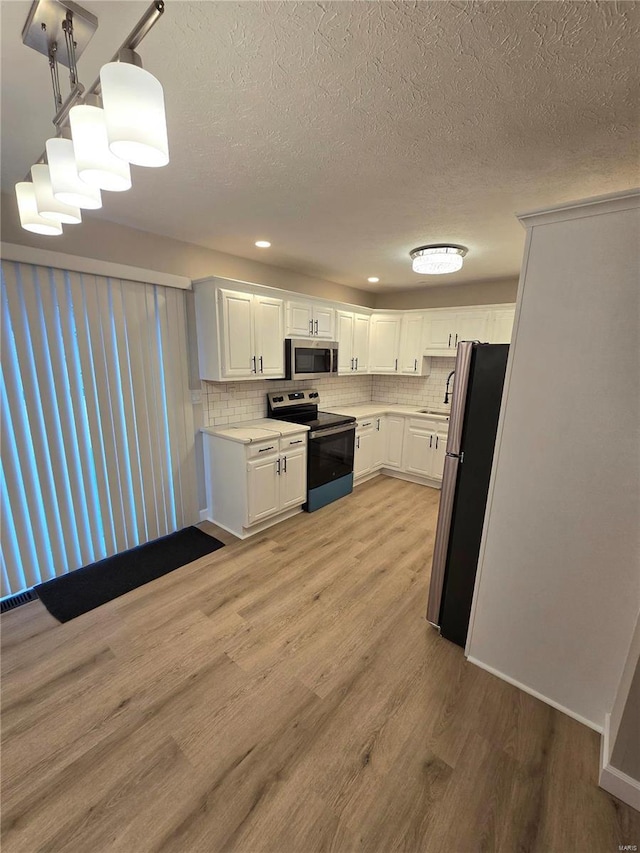 kitchen with pendant lighting, stainless steel appliances, white cabinets, decorative backsplash, and light wood-type flooring