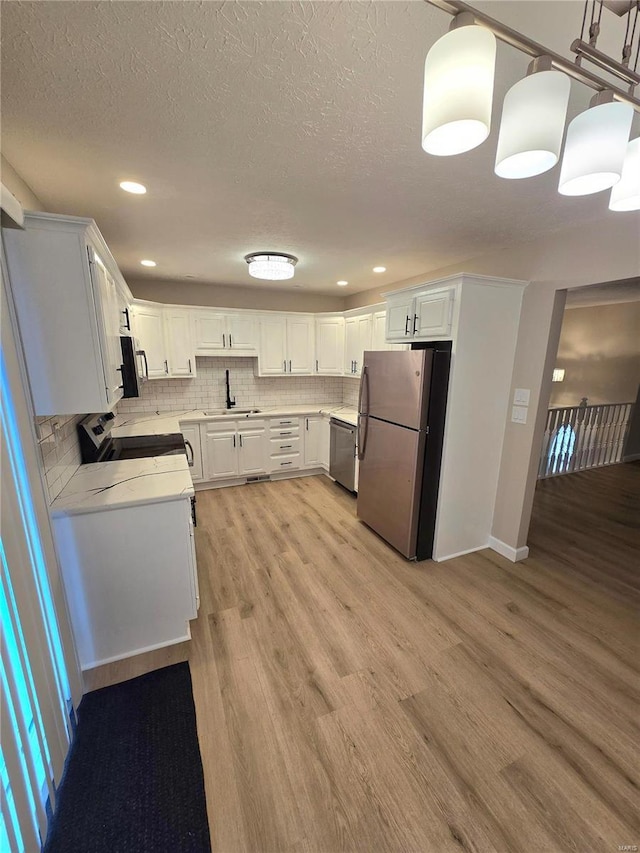 kitchen featuring appliances with stainless steel finishes, tasteful backsplash, white cabinetry, sink, and light wood-type flooring