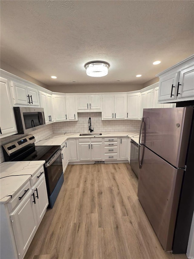 kitchen with sink, light hardwood / wood-style flooring, appliances with stainless steel finishes, white cabinetry, and light stone countertops