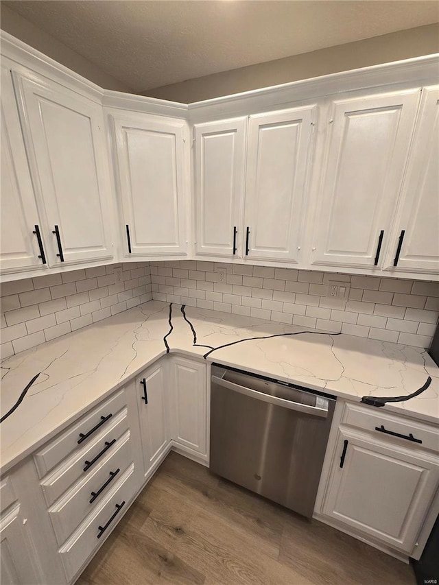 kitchen featuring dishwasher, white cabinetry, hardwood / wood-style floors, backsplash, and light stone countertops