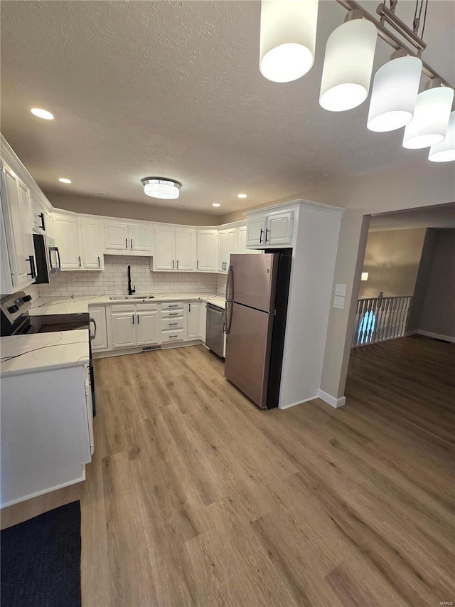 kitchen featuring tasteful backsplash, appliances with stainless steel finishes, light hardwood / wood-style flooring, and white cabinets