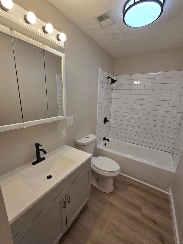 full bathroom with tiled shower / bath, hardwood / wood-style floors, vanity, toilet, and a textured ceiling