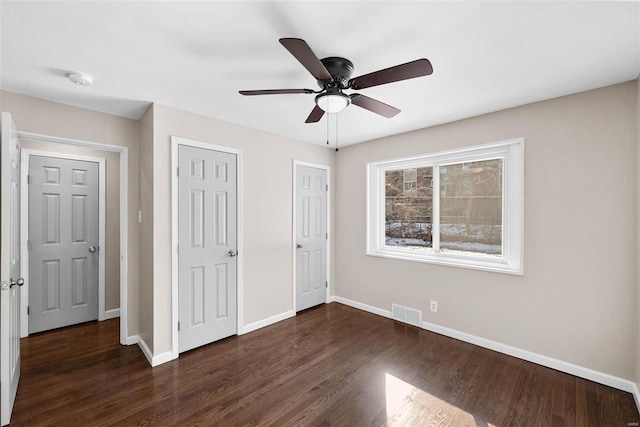 unfurnished bedroom featuring visible vents, baseboards, dark wood finished floors, ceiling fan, and two closets