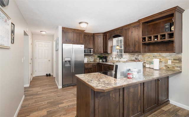 kitchen with dark brown cabinetry, decorative backsplash, kitchen peninsula, and appliances with stainless steel finishes