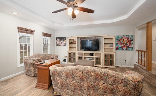 living room with ceiling fan, a tray ceiling, and light hardwood / wood-style floors