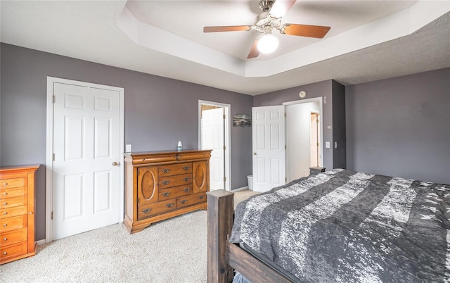 bedroom featuring ceiling fan, light colored carpet, and a tray ceiling