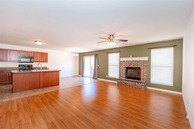 kitchen with ceiling fan with notable chandelier, open floor plan, a brick fireplace, black appliances, and light wood finished floors