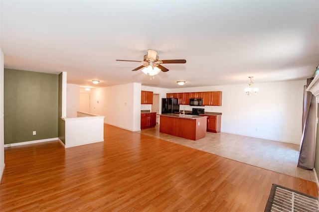 kitchen with an island with sink, light wood-style flooring, open floor plan, black appliances, and ceiling fan with notable chandelier