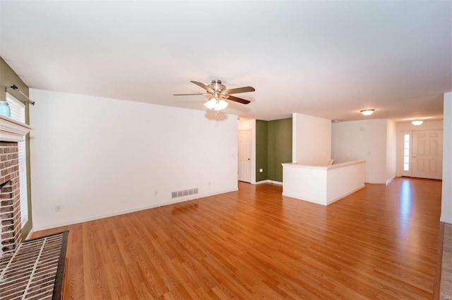 unfurnished living room with visible vents, baseboards, a ceiling fan, light wood-style flooring, and a brick fireplace