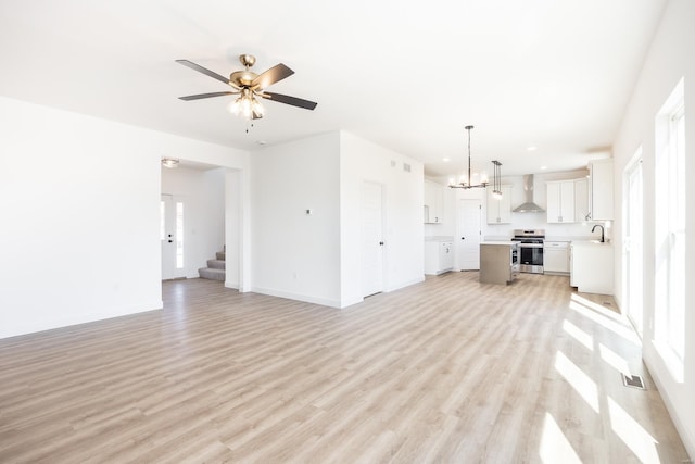 unfurnished living room with baseboards, stairway, light wood-style flooring, ceiling fan with notable chandelier, and a sink