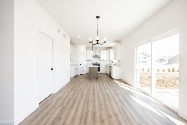 kitchen featuring light wood-style floors, appliances with stainless steel finishes, white cabinets, an inviting chandelier, and baseboards