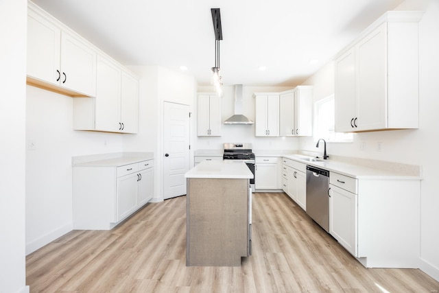 kitchen with a center island, appliances with stainless steel finishes, light wood-style floors, wall chimney exhaust hood, and a sink