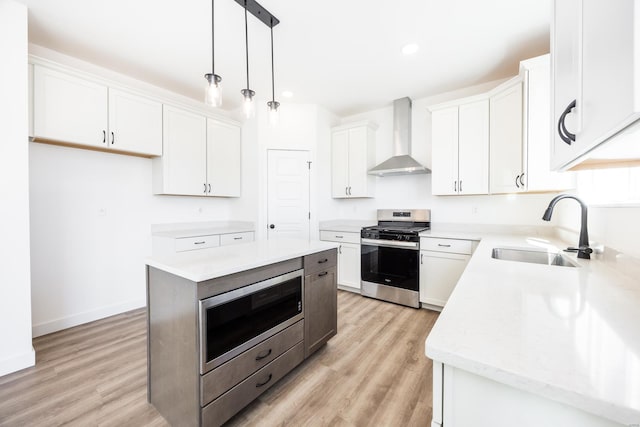 kitchen with wall chimney range hood, light countertops, stainless steel appliances, white cabinetry, and a sink