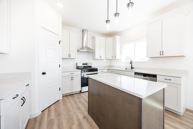 kitchen with wall chimney range hood, light wood-type flooring, white cabinets, stainless steel appliances, and a sink