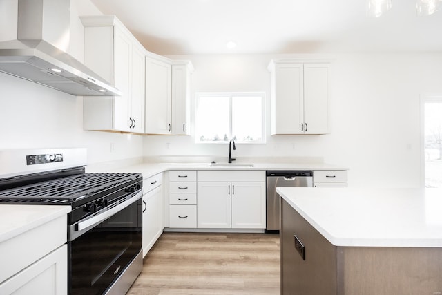 kitchen with a sink, white cabinets, light wood-style floors, appliances with stainless steel finishes, and wall chimney exhaust hood