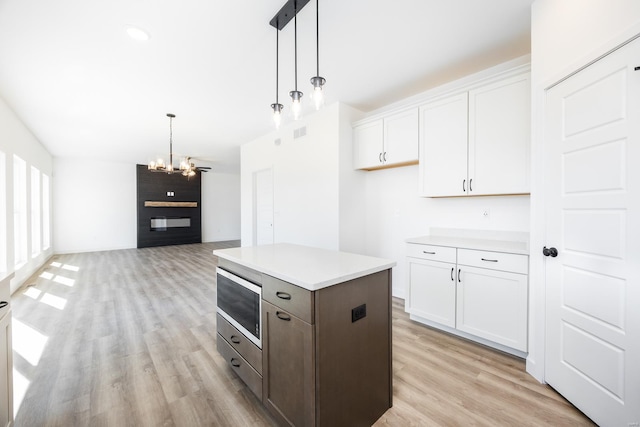 kitchen with light wood-style floors, pendant lighting, white cabinetry, stainless steel microwave, and a notable chandelier