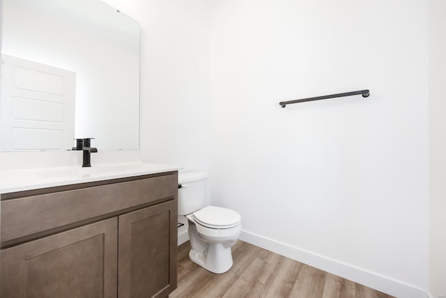 bathroom with vanity, toilet, wood finished floors, and baseboards