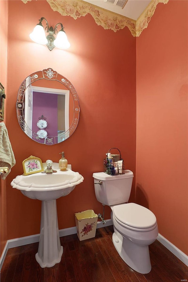 half bath with toilet, wood-type flooring, visible vents, and baseboards