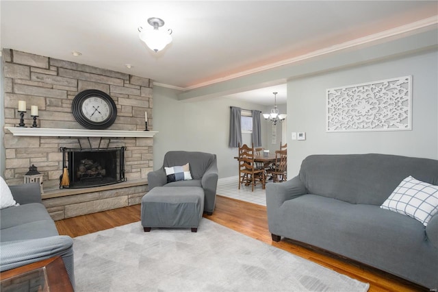 living area with a notable chandelier, ornamental molding, wood finished floors, and a stone fireplace