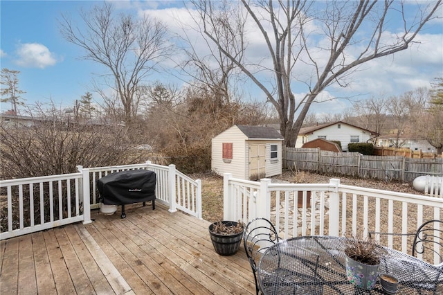 wooden terrace featuring an outbuilding, a grill, fence, a shed, and outdoor dining space