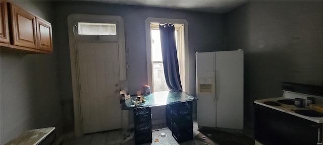 kitchen featuring brown cabinetry, a healthy amount of sunlight, range with electric stovetop, and white refrigerator with ice dispenser