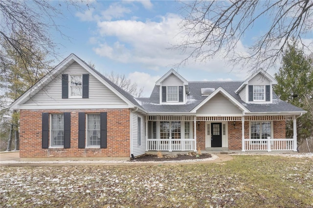 new england style home featuring brick siding, covered porch, and a shingled roof