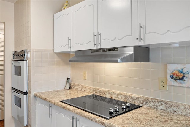 kitchen with tasteful backsplash, white cabinets, white double oven, black electric stovetop, and light stone countertops