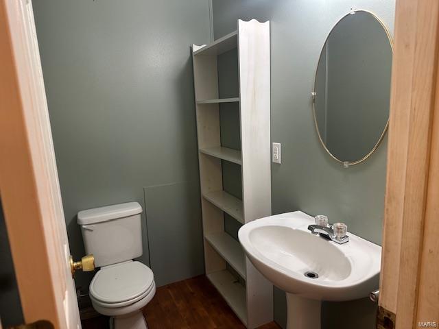 half bath featuring wood finished floors, toilet, and a sink