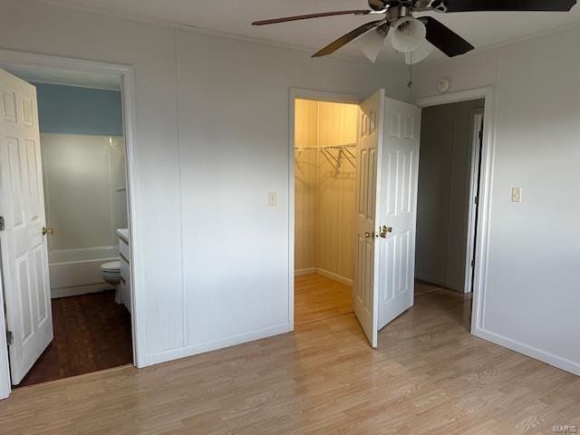 unfurnished bedroom with a closet, light wood finished floors, baseboards, ceiling fan, and a walk in closet