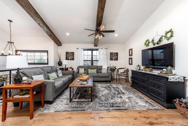 living room with ceiling fan with notable chandelier, hardwood / wood-style floors, and vaulted ceiling with beams