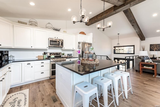 kitchen with white cabinets, appliances with stainless steel finishes, a kitchen breakfast bar, and a notable chandelier