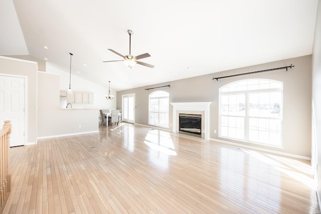 unfurnished living room featuring ceiling fan with notable chandelier, light hardwood / wood-style flooring, vaulted ceiling, and a high end fireplace