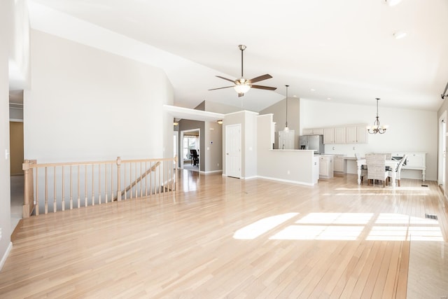 unfurnished living room with ceiling fan with notable chandelier, light hardwood / wood-style floors, and high vaulted ceiling