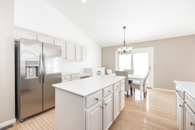 kitchen with lofted ceiling, pendant lighting, stainless steel fridge, a kitchen island, and white cabinetry